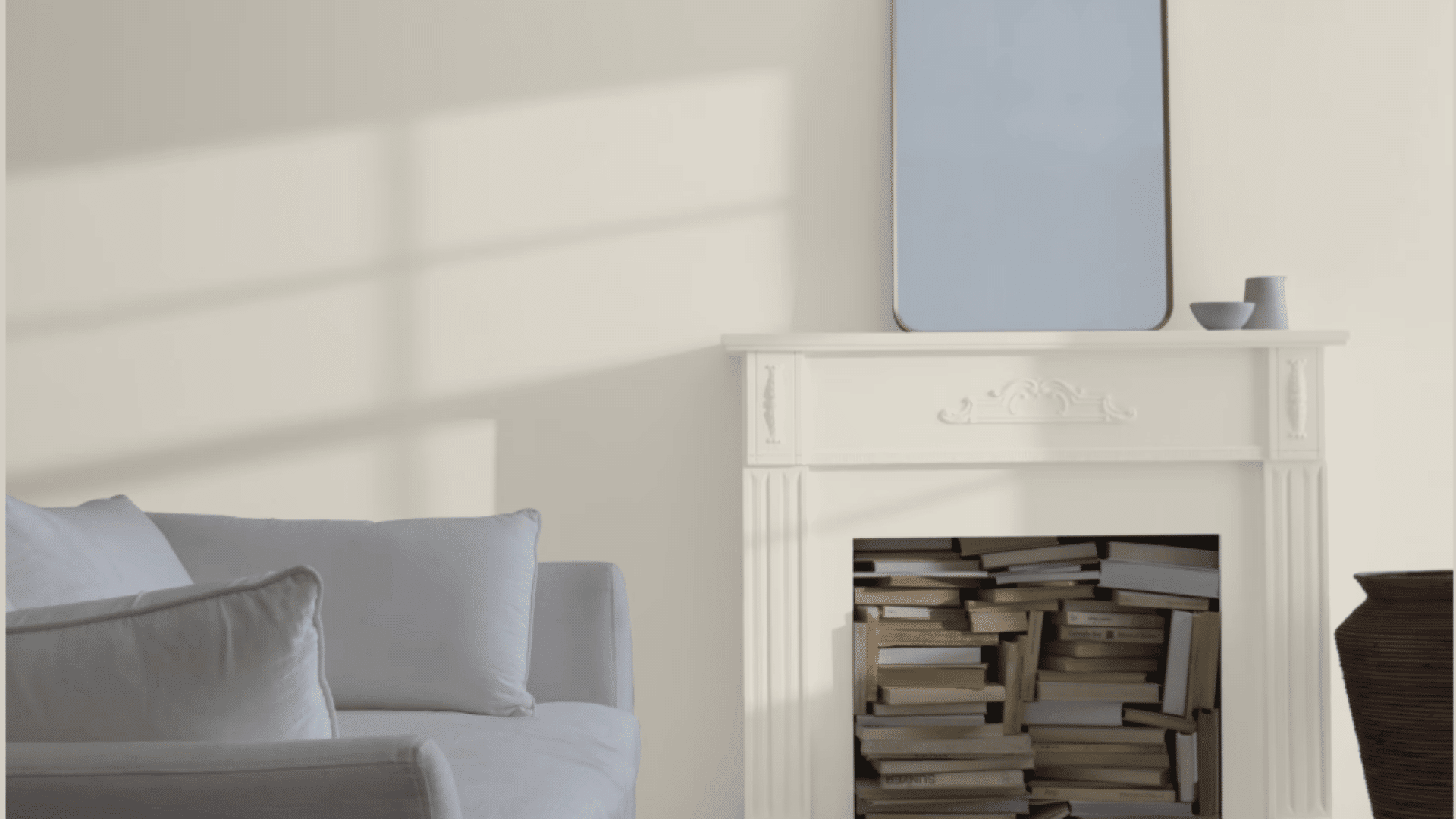 Cream fireplace with stacked books, wall mirror, and white sofa in a bright BM Collingwood painted living room