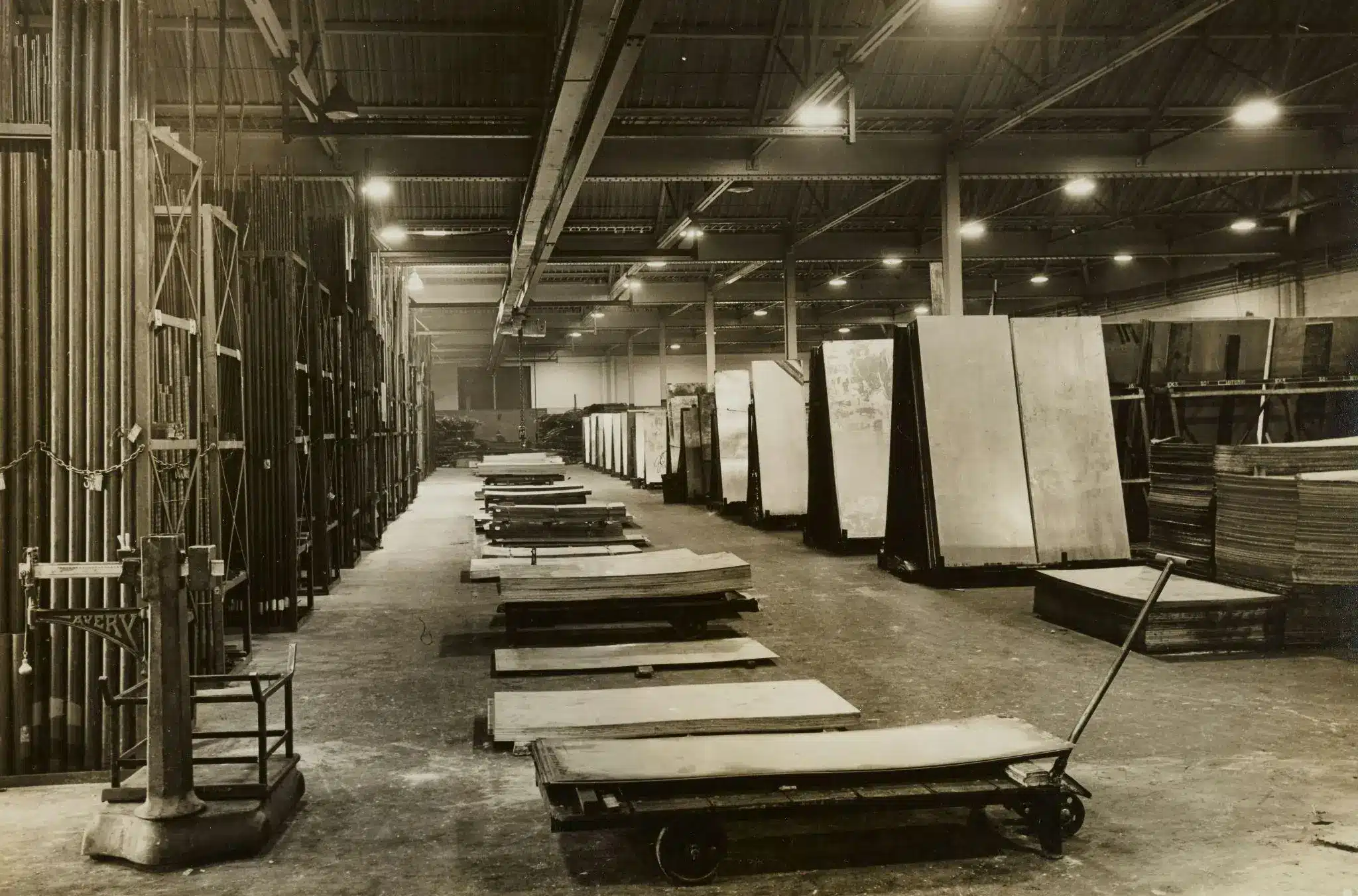 Large warehouse interior with stacks of metal sheets and wooden carts on concrete floor