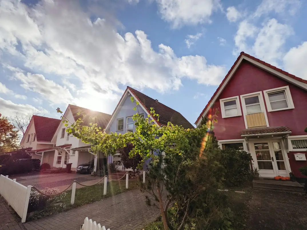 Row of colorful suburban houses under blue sky with trees and white picket fence