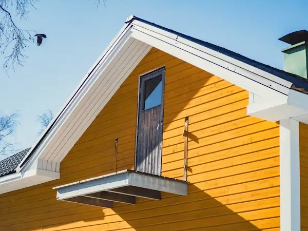 Orange gabled house exterior with a door leading to a balcony and a blue sky background