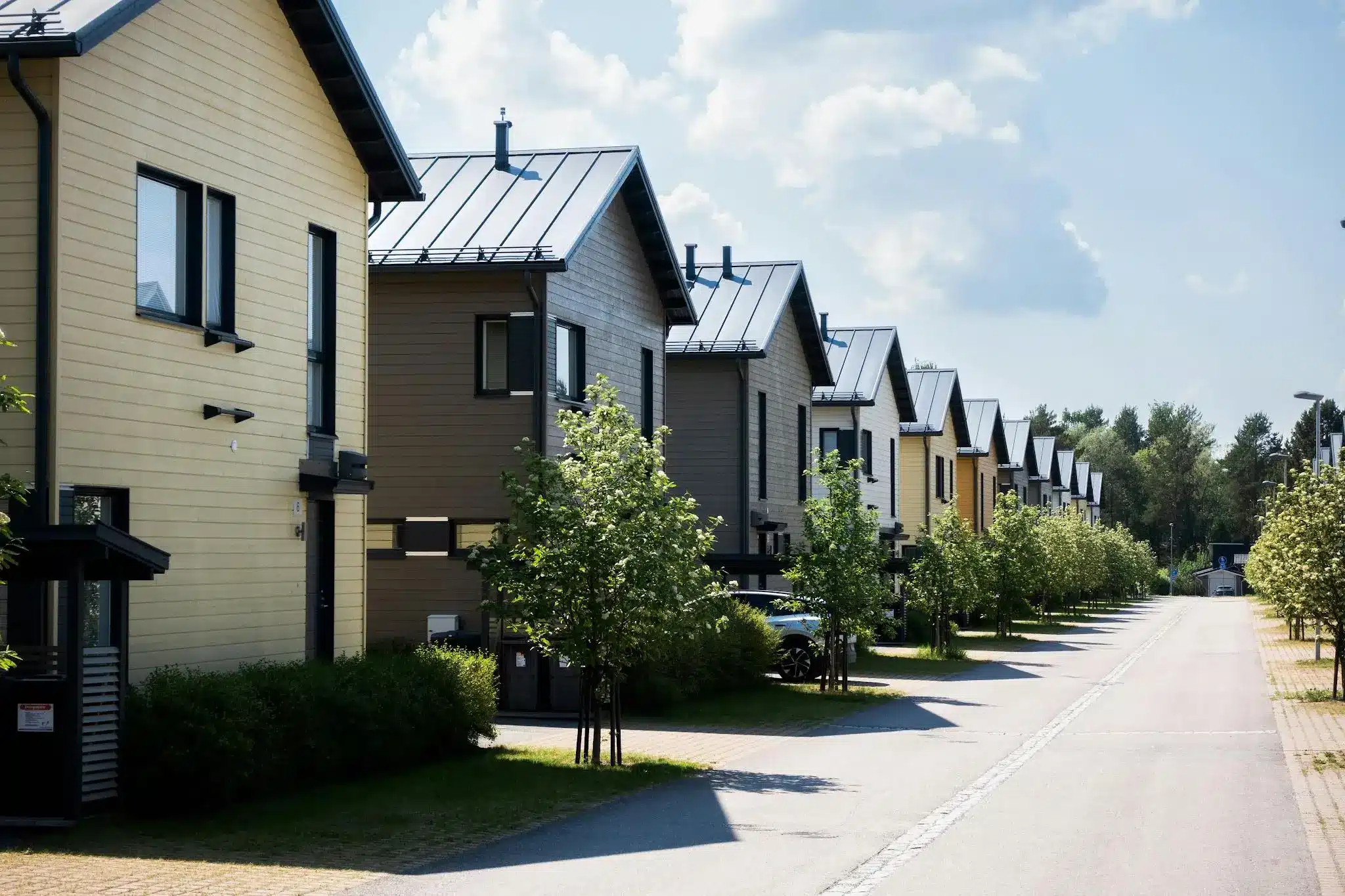 Row of modern suburban houses with metal roofs lining a sunny tree-lined street