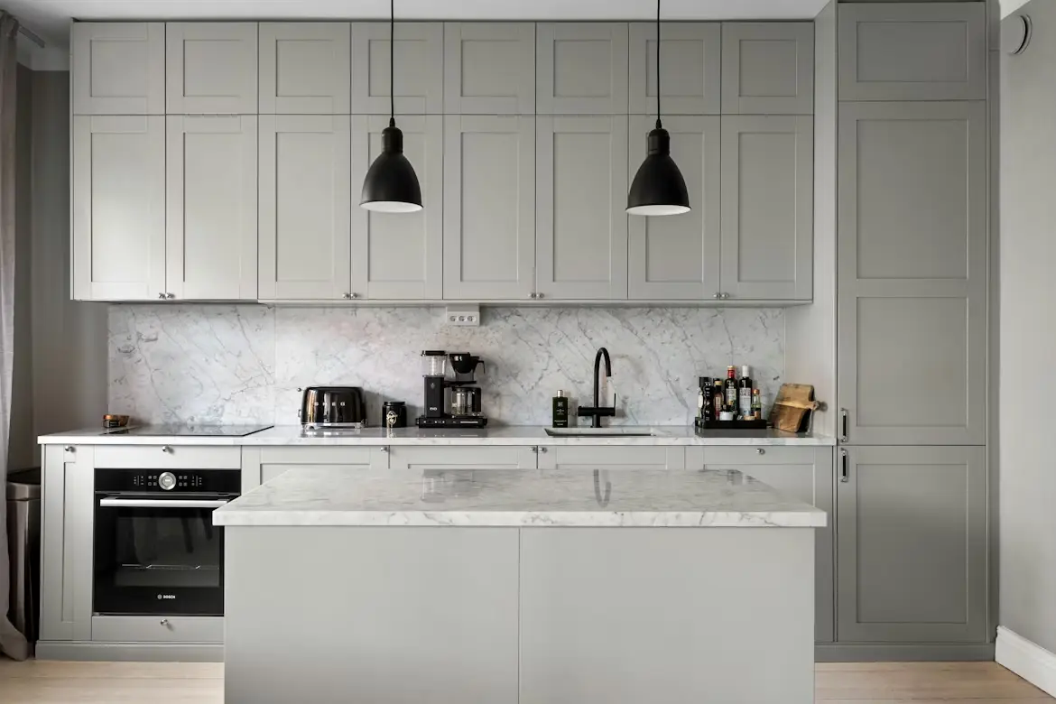 Modern kitchen with gray cabinets, marble countertop, and black pendant lights