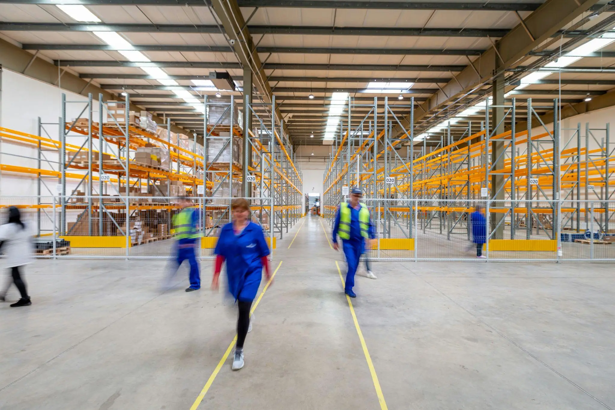 Workers in blue uniforms walking inside a large warehouse with empty metal shelves