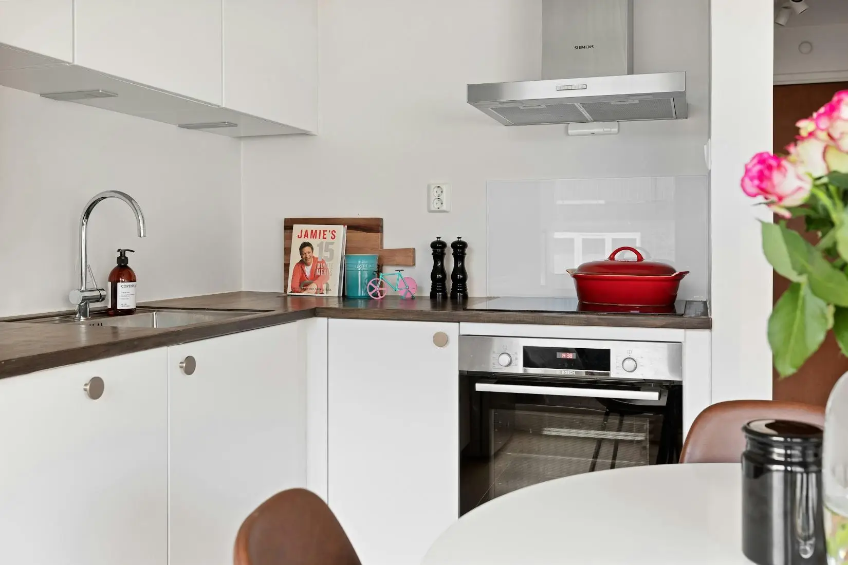Modern kitchen with red pot on stove, cookbook, and flowers on table