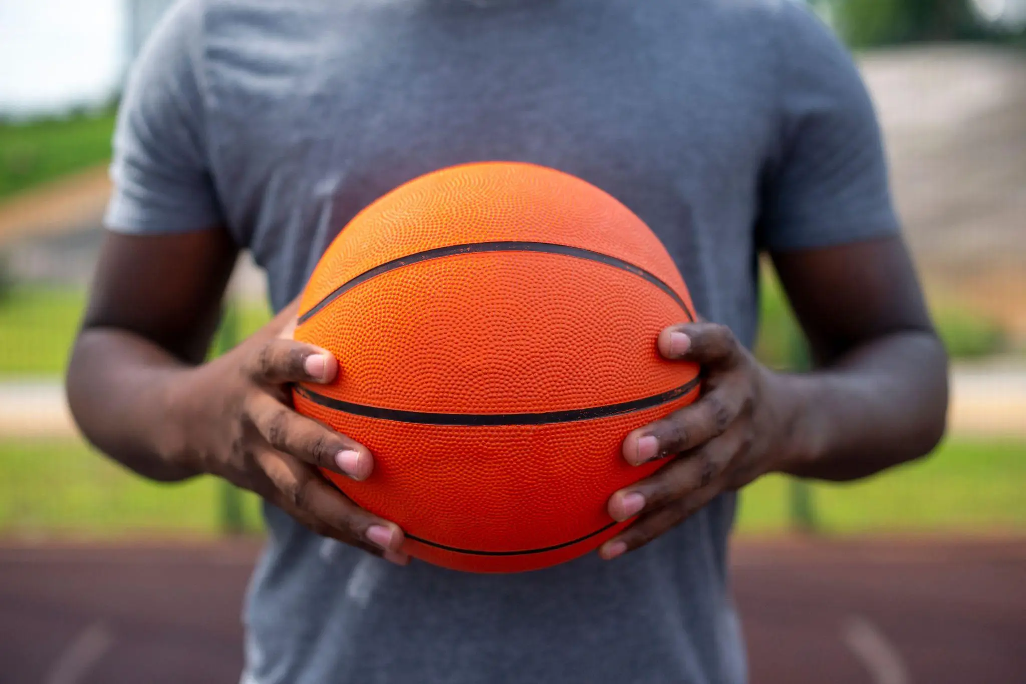 Person holding an orange basketball on outdoor court wearing a gray shirt