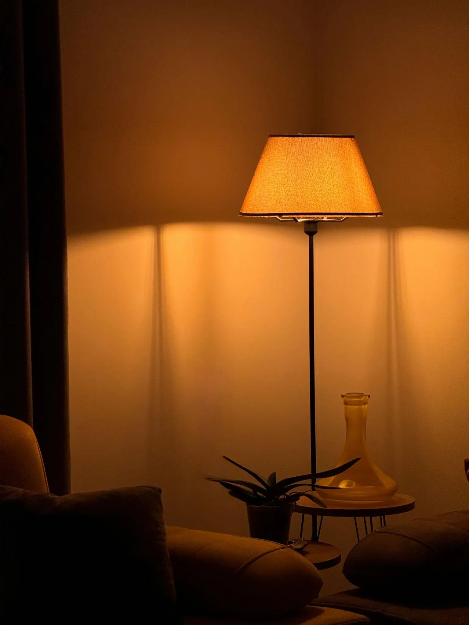 Warmly lit lamp casting shadows in cozy living room with yellow sofa and side table