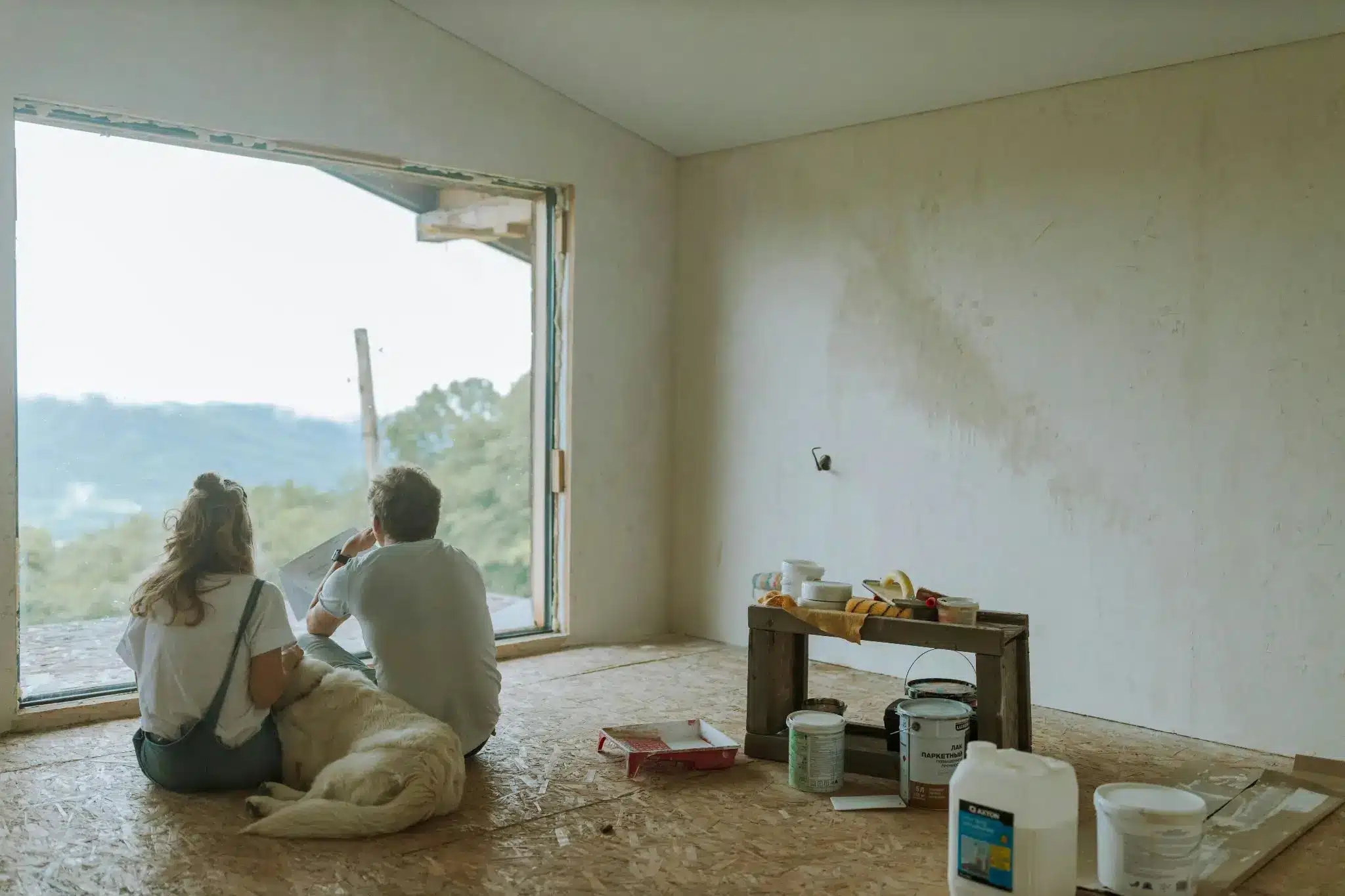 Couple sitting with dog in unfinished room overlooking scenic landscape