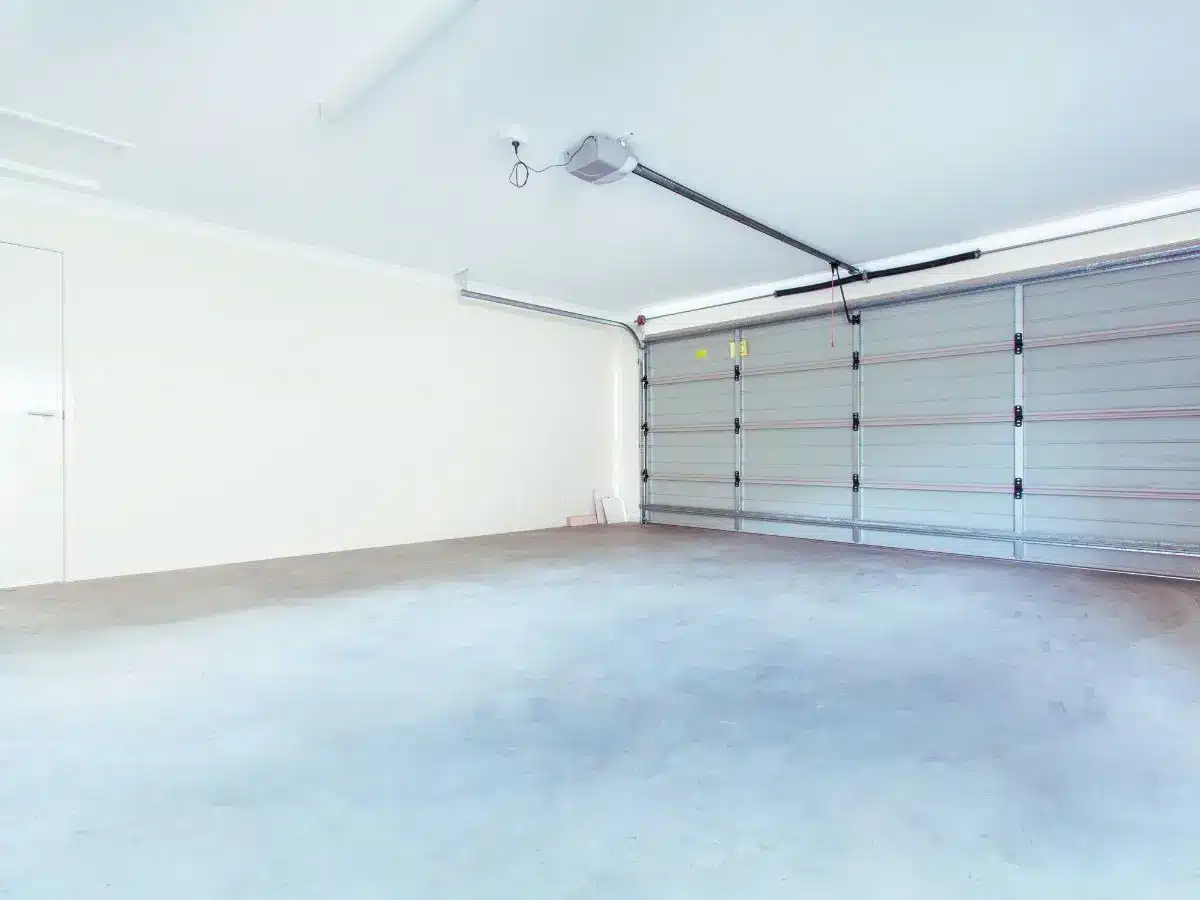 Spacious empty garage with concrete floor and closed roller door under bright overhead lighting