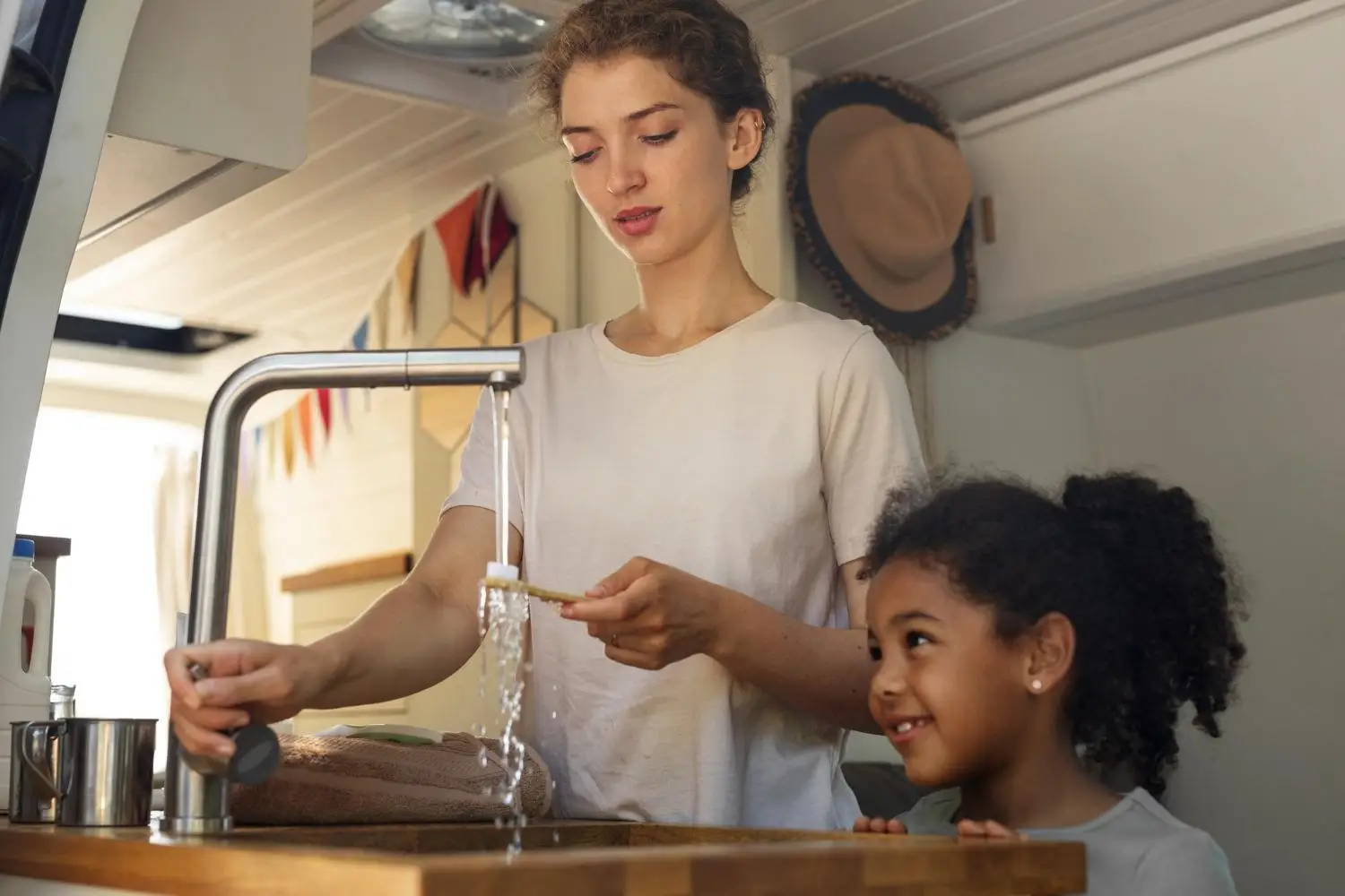 Woman washing dish in camper van kitchen with child watching nearby