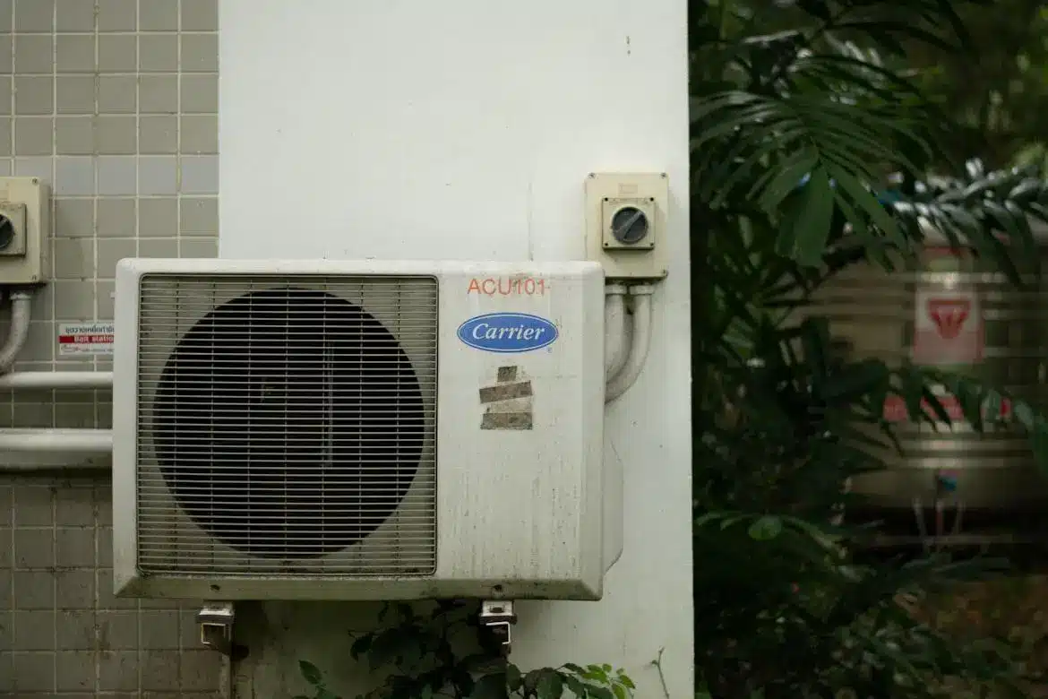 Outdoor air conditioning unit mounted on wall beside foliage