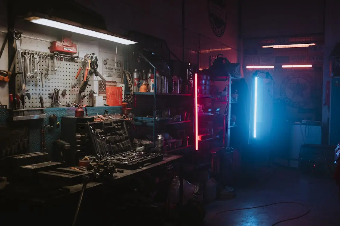 Industrial workshop with tools on wall and workbenches illuminated by red and blue neon lights