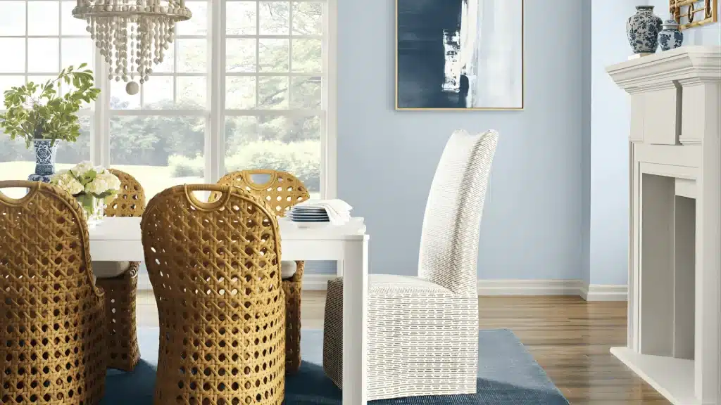 Light blue dining room with woven chairs, white table, fireplace, and bright natural window light