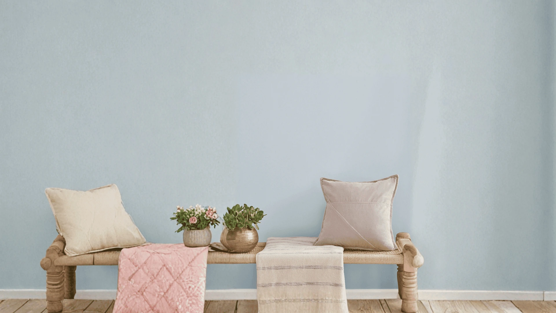 Minimal bench with cushions, soft blue wall, plants, and natural wood floor in airy interior