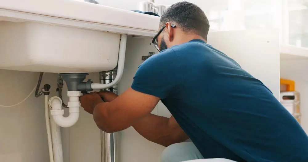Man fixing pipes under a kitchen sink in a bright room
