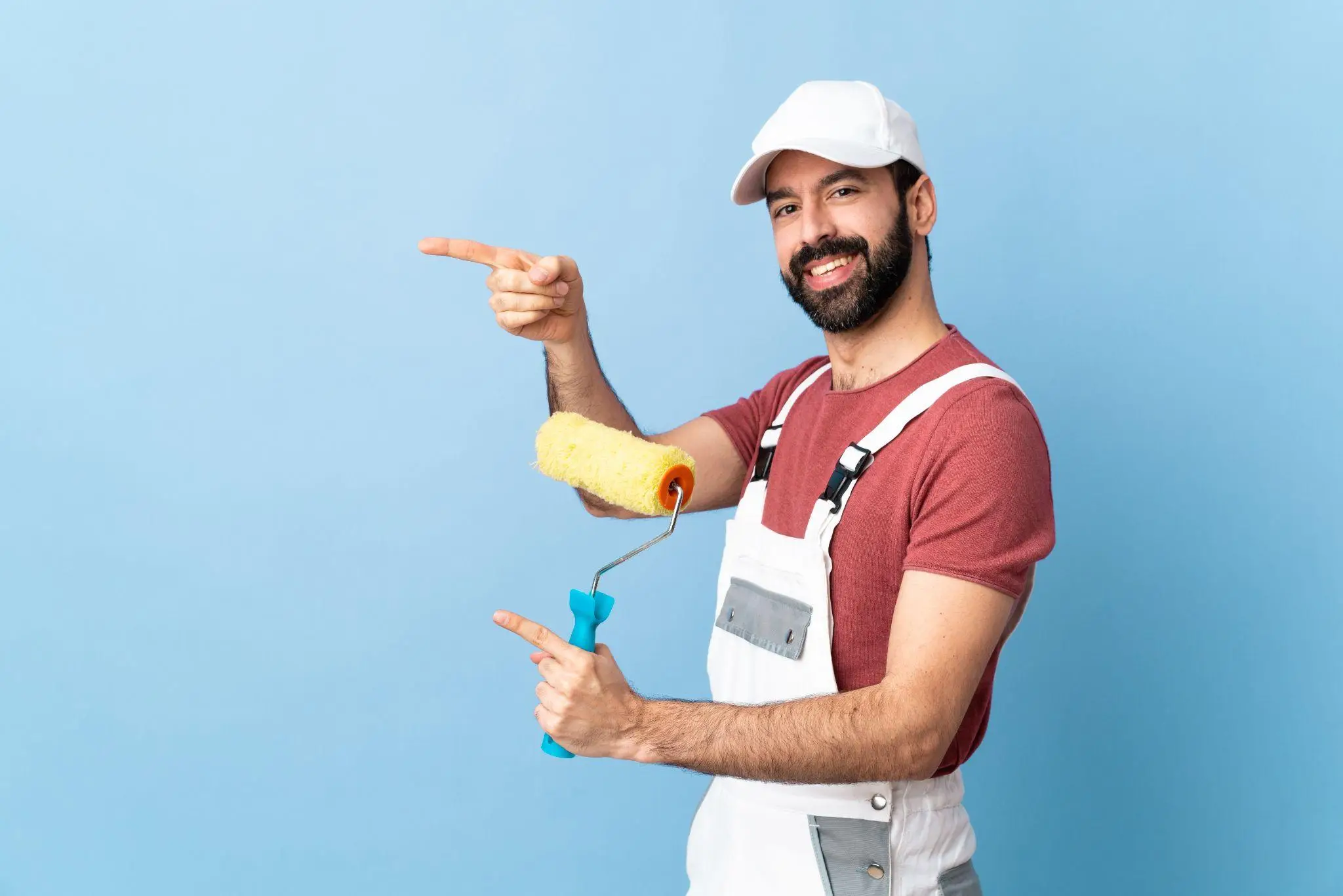 Painter in white overalls holding paint roller against blue background