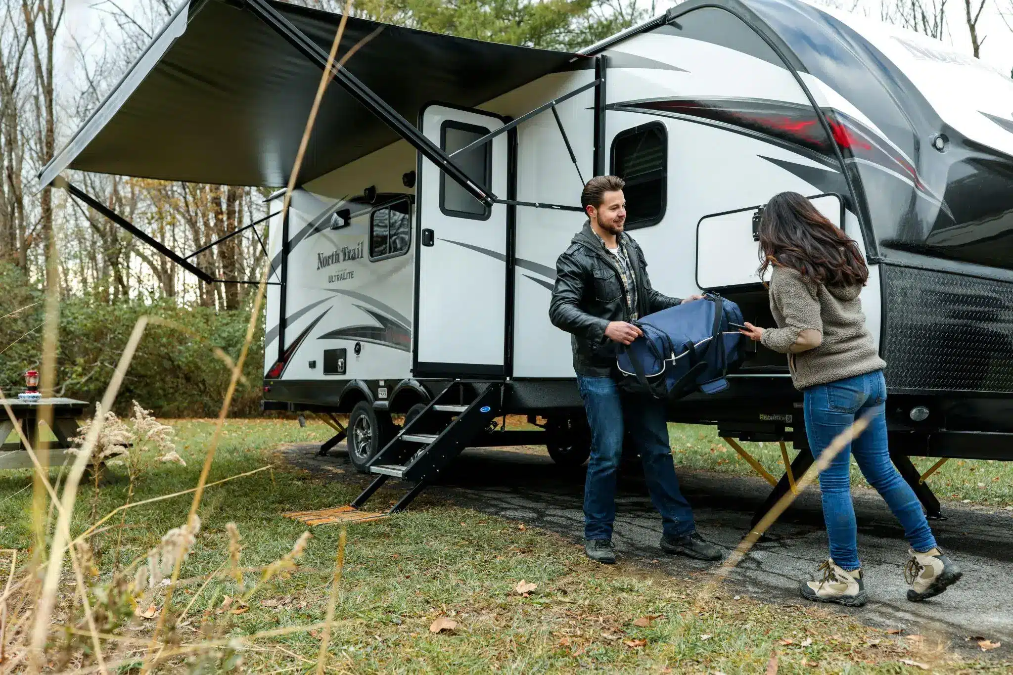 Couple unpacking luggage from modern camper trailer at a forest campsite