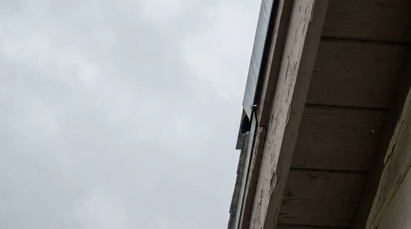 Weathered wooden eaves with metal reinforcement under overcast sky