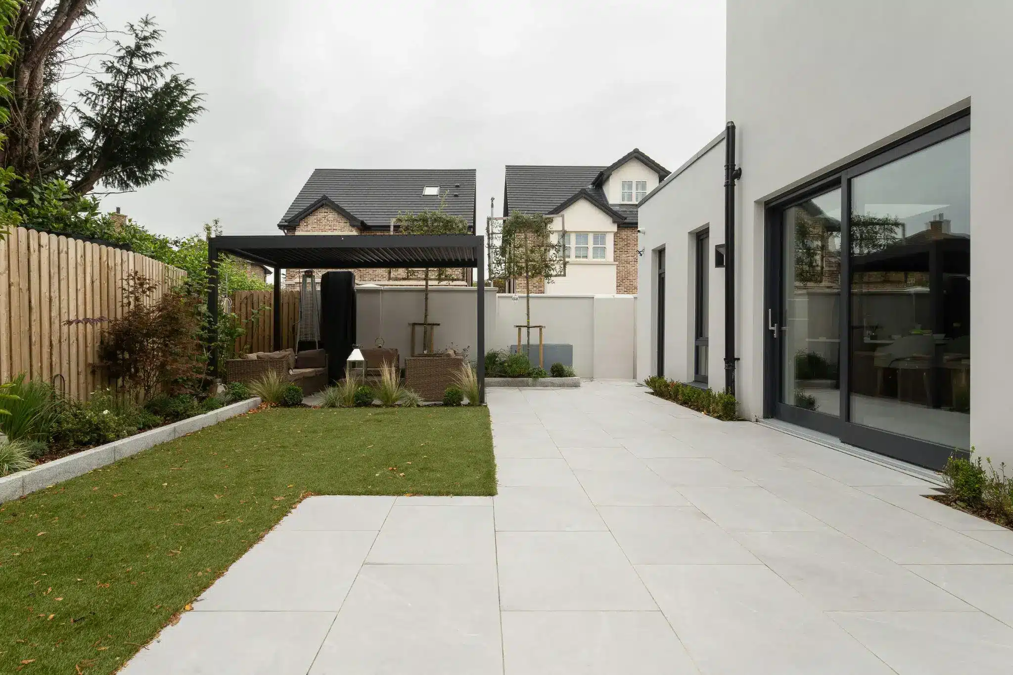 Modern patio with pergola, wicker furniture, and lush garden in suburban backyard setting