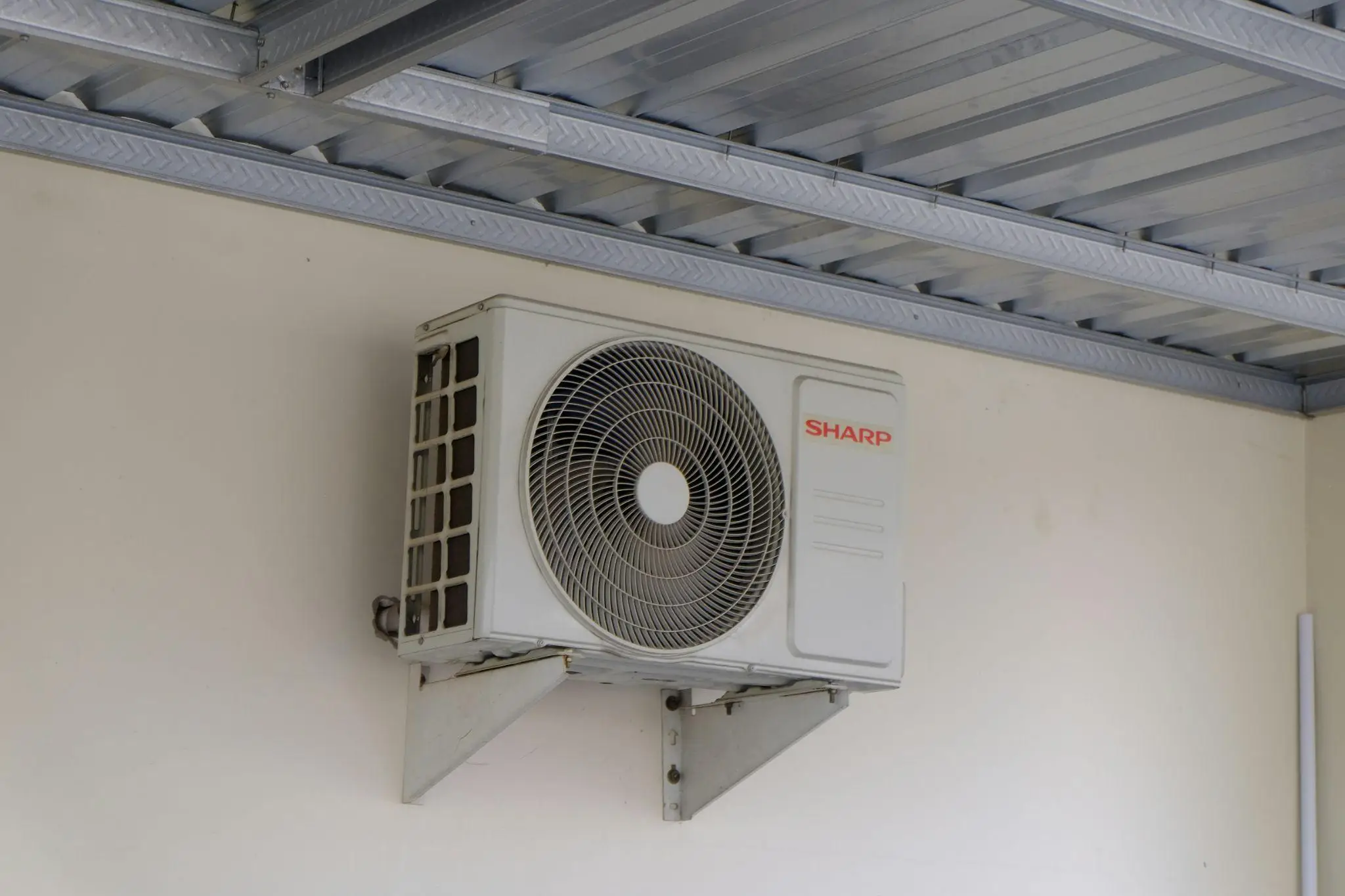 Wall-mounted air conditioning unit in an industrial setting with metal ceiling beams