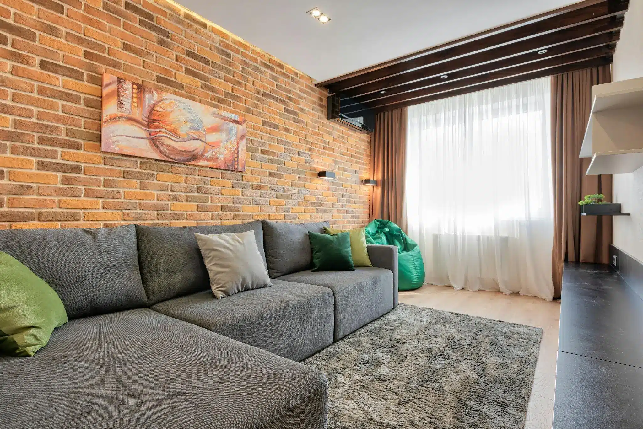Gray sectional sofa with green pillows in modern living room with brick accent wall