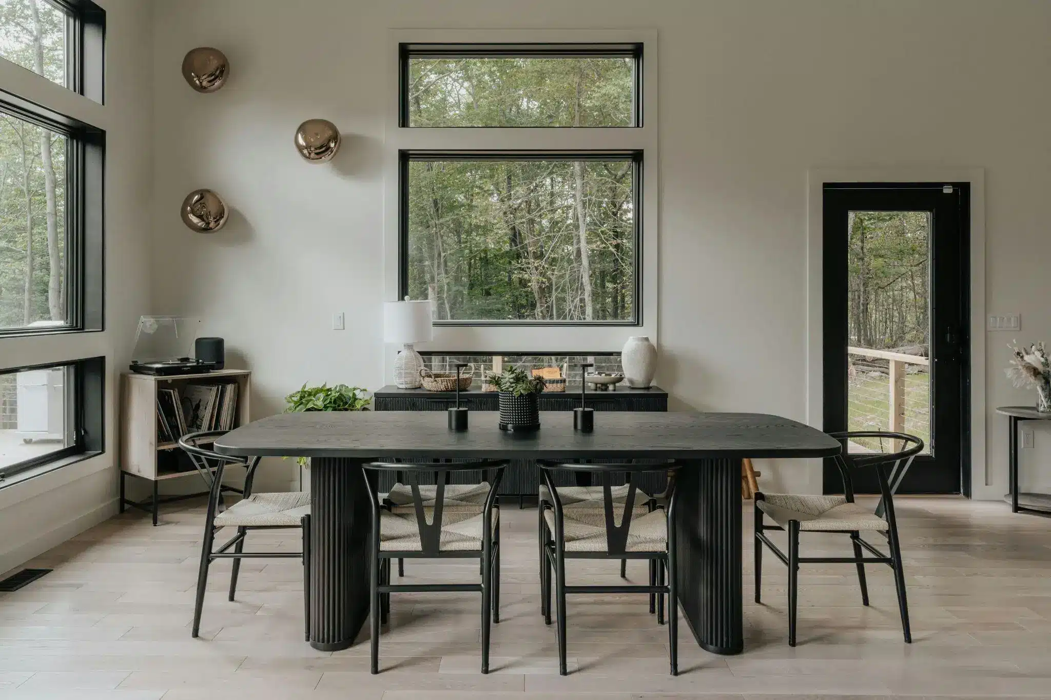 Modern dining room with black table and chairs, large windows, and natural daylight filtering in