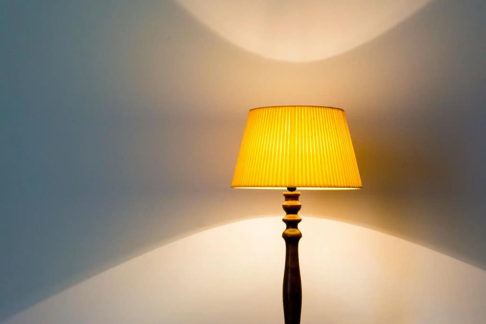 A wooden floor lamp with a yellow lampshade casting shadows on a wall