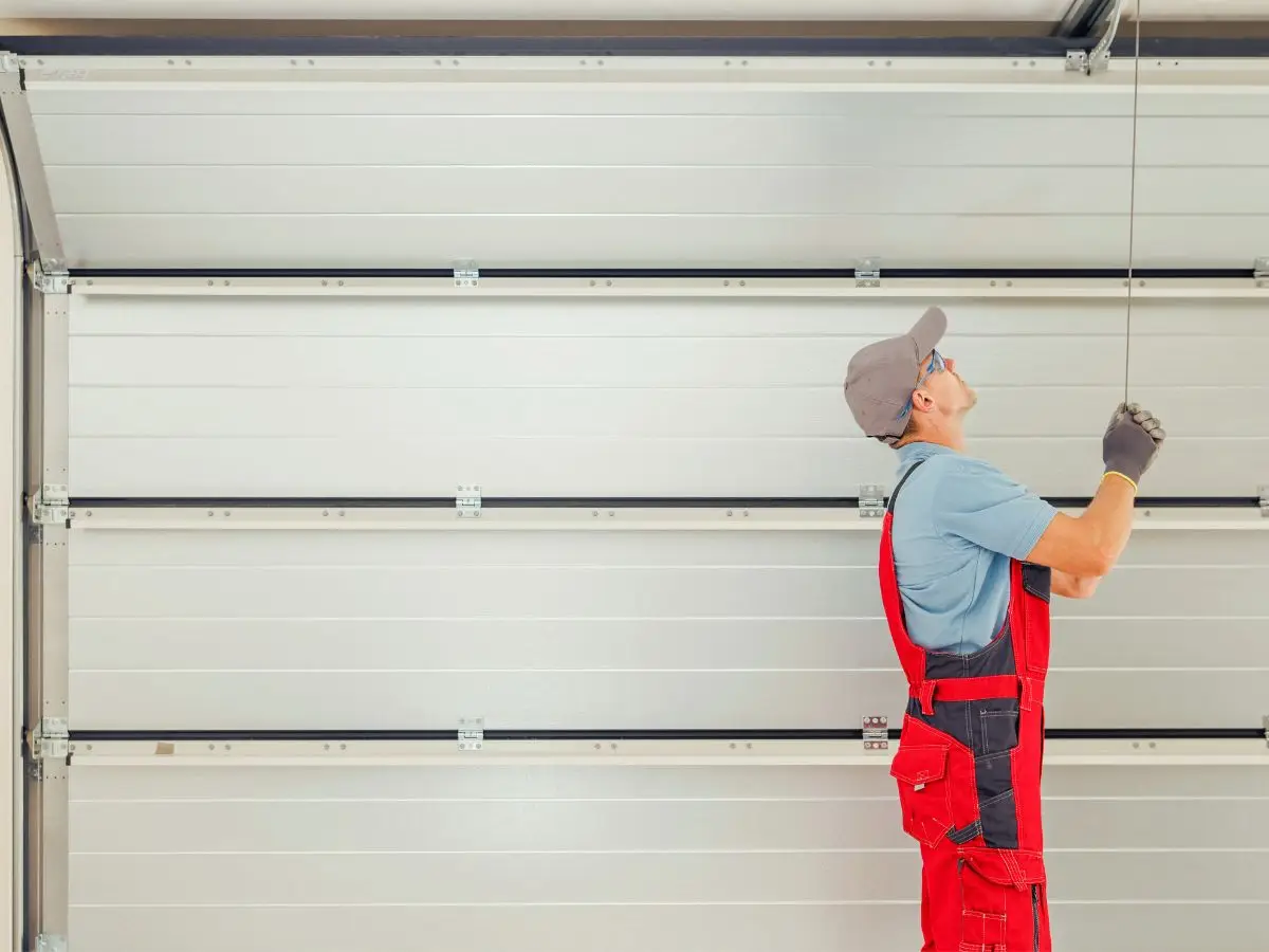 Worker in red overalls repairing garage door mechanism indoors
