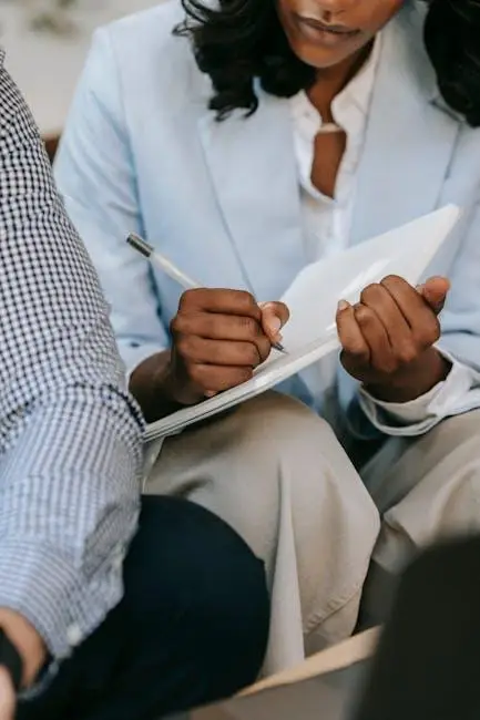 Person in light blue blazer taking notes on pad with pen in office setting