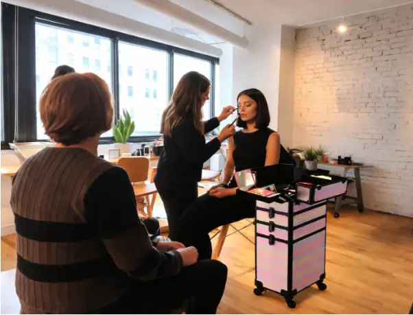 Makeup artist applying cosmetics to a woman in a bright studio with wooden floors