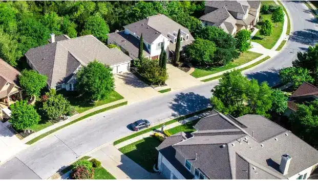Aerial view of suburban neighborhood with tree-lined streets and cars parked in driveways