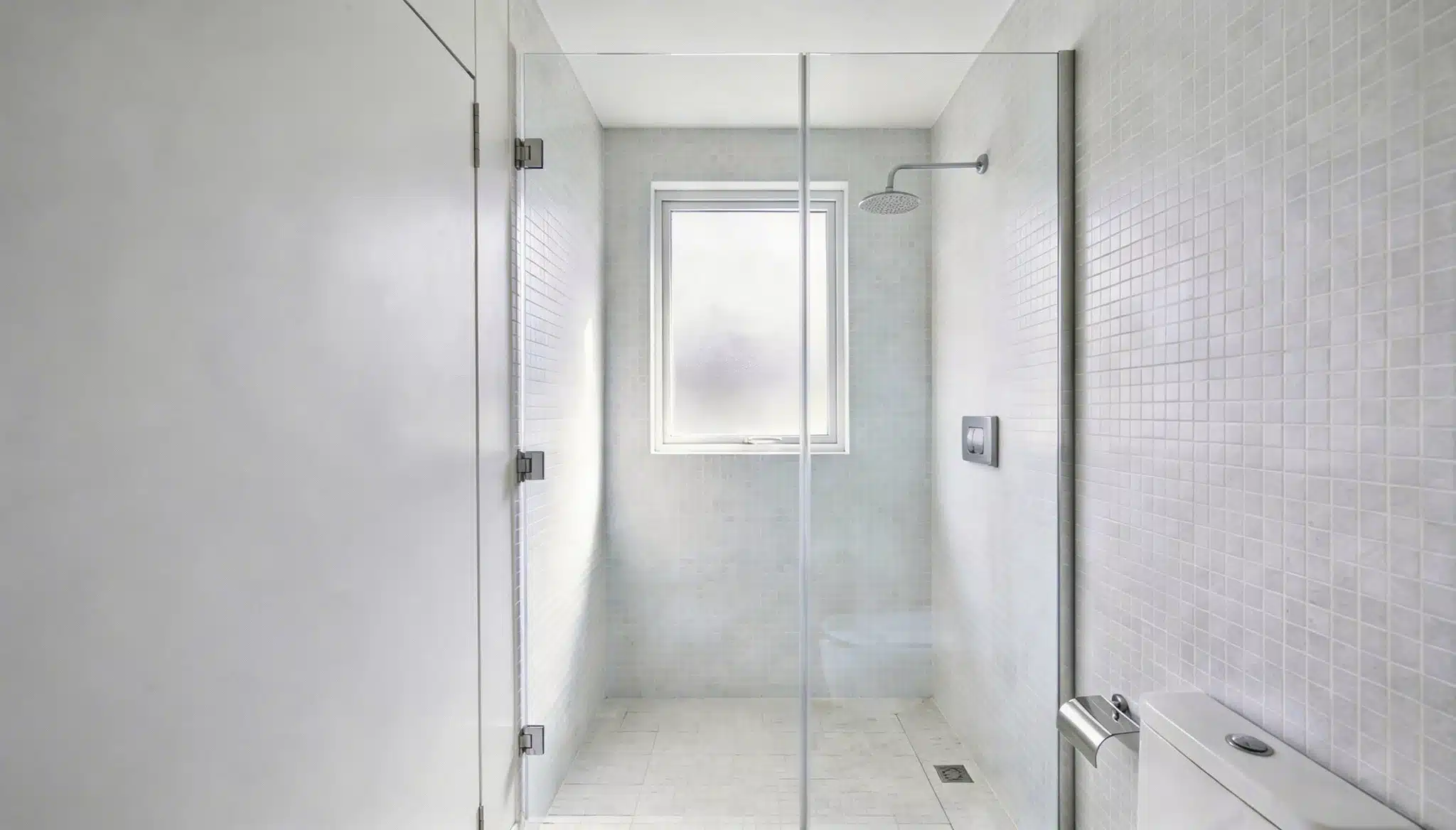 Minimalist bathroom featuring a walk-in shower enclosed by frameless glass white mosaic tile walls and a frosted window