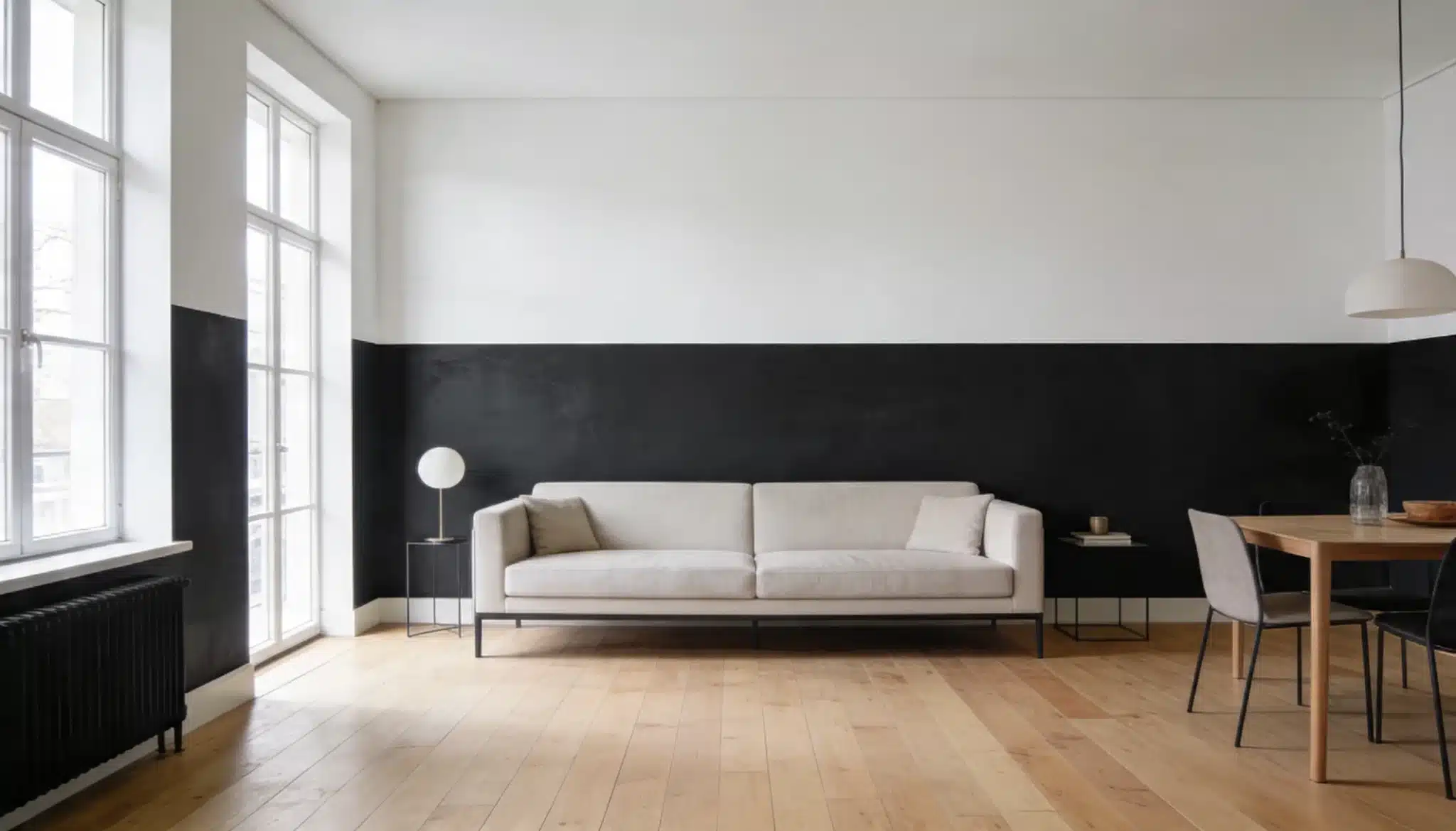 Minimalist living and dining space featuring a beige sofa centered against a black and white two-toned wall light wood floors and tall windows