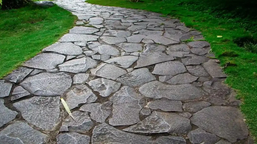 Stepping stone garden path constructed of irregularly shaped, gray flagstones bordered by lush green grass