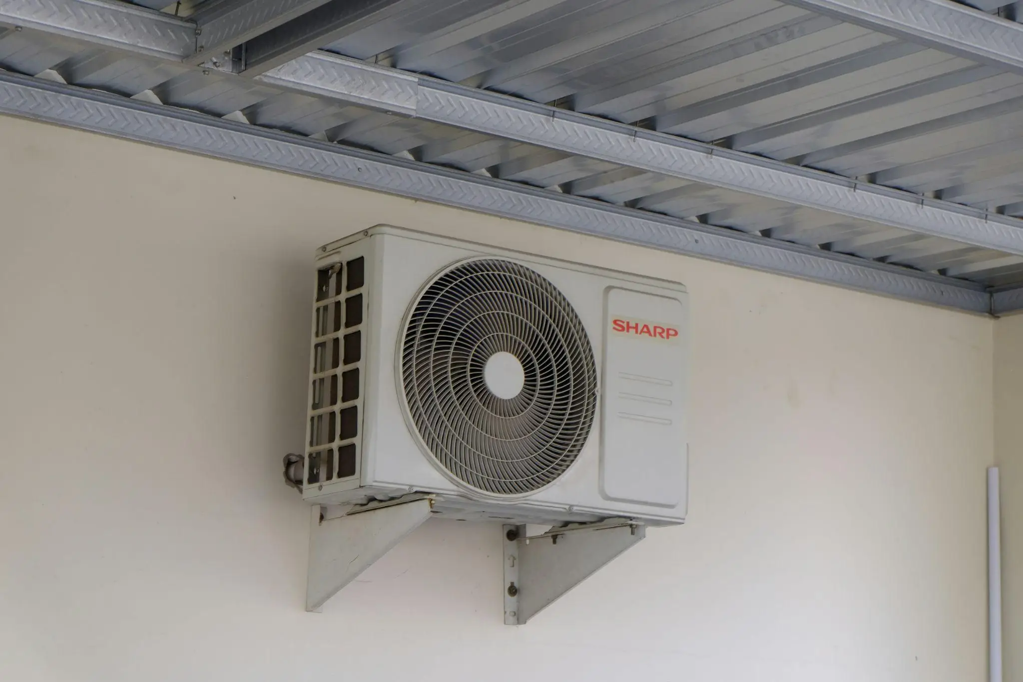 External air conditioning unit mounted on beige wall under metal roof structure