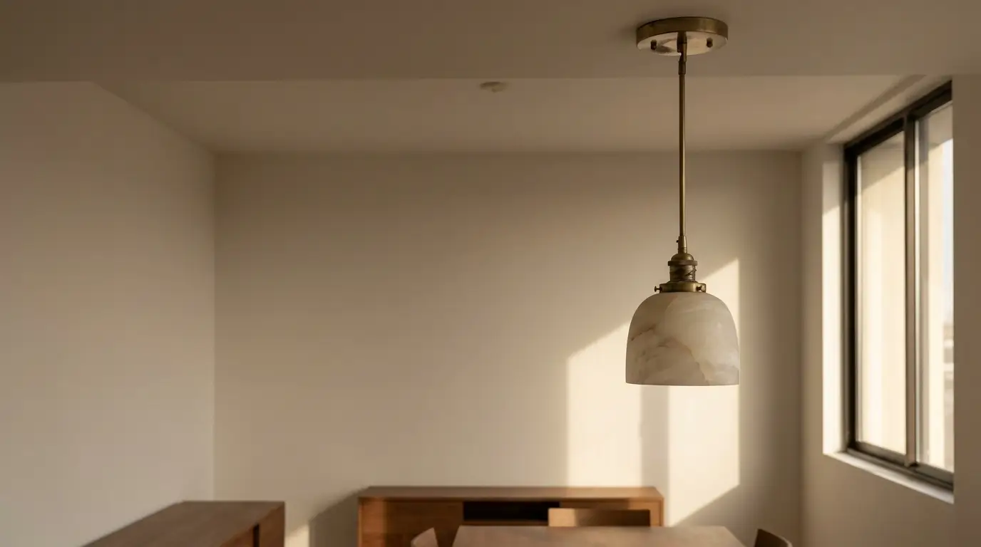 Pendant light with brass fixture in minimalist dining room with wooden furniture and natural light