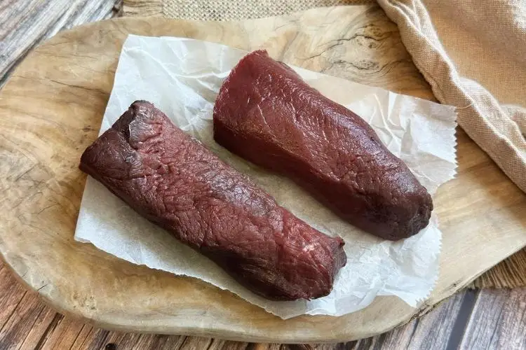 Two raw beef tenderloin steaks on parchment paper over rustic wooden board