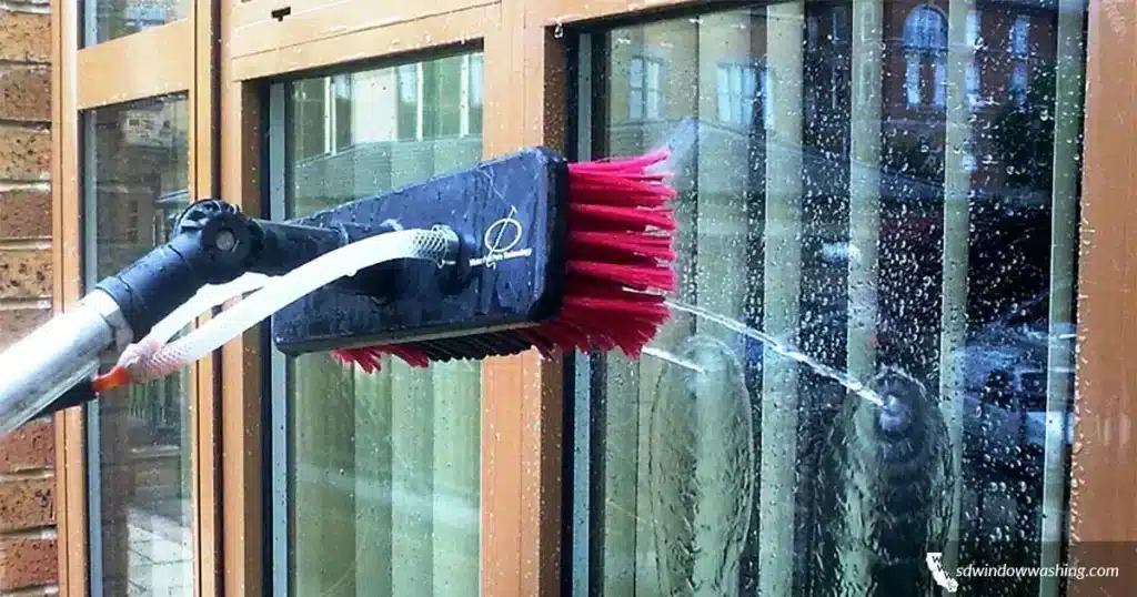 Brush with red bristles cleaning glass window with water spray in an outdoor setting