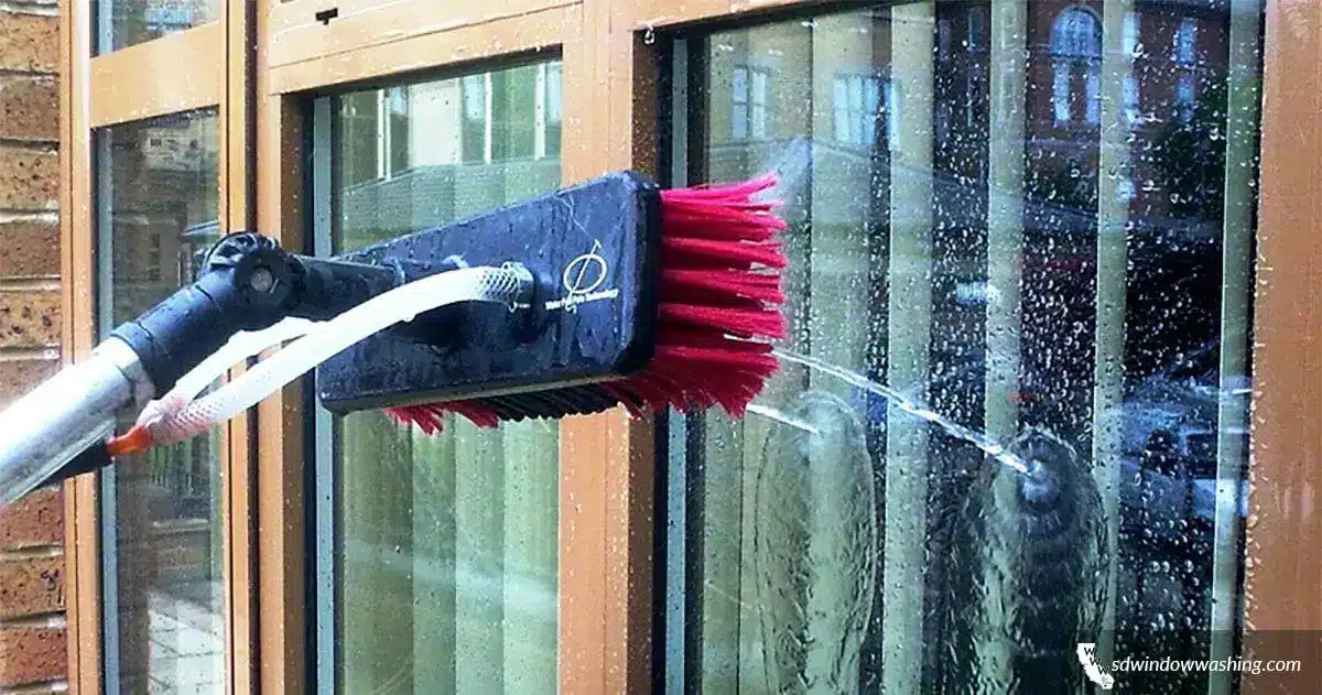 Brush with red bristles cleaning glass window with water spray in an outdoor setting