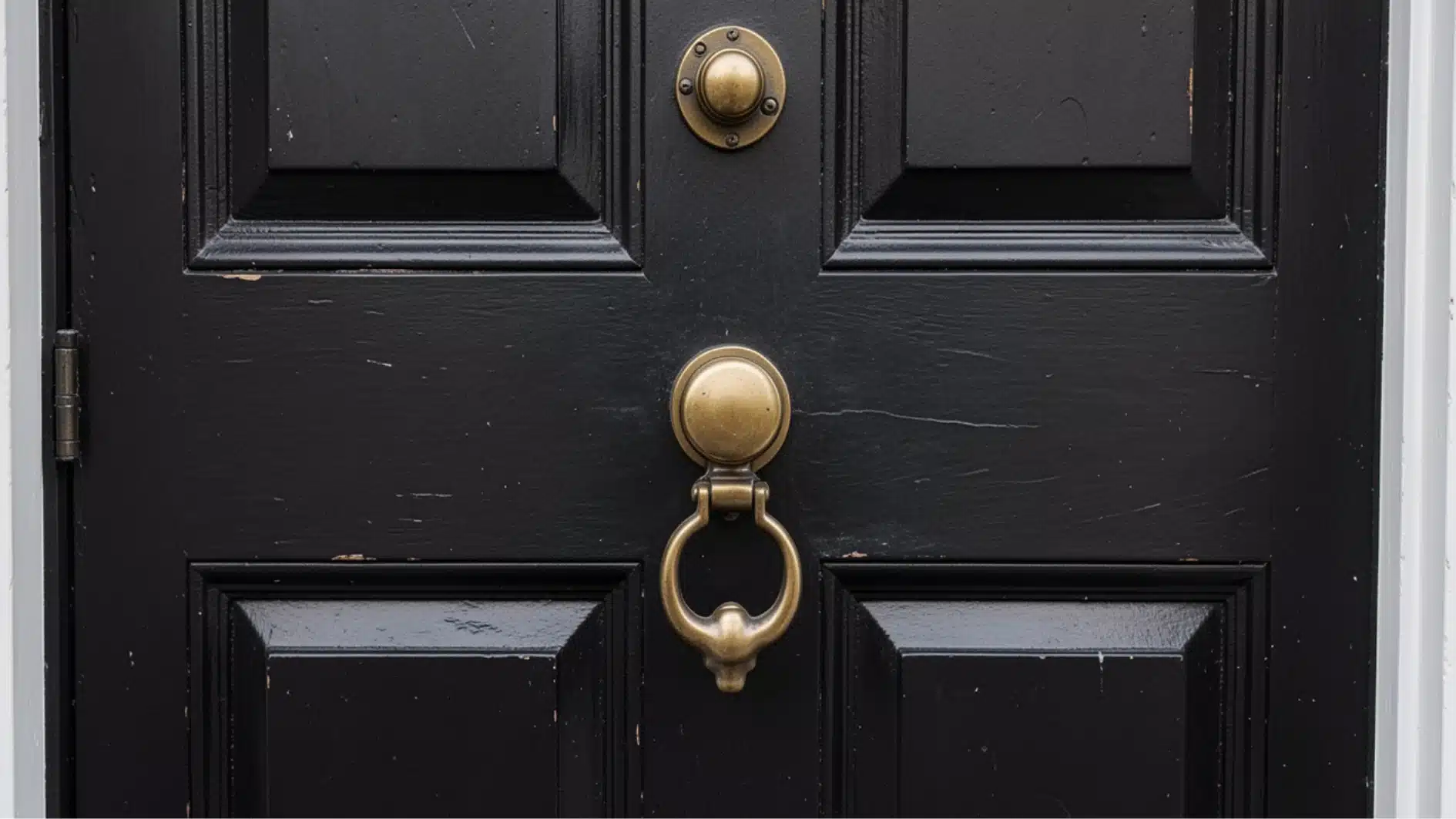 Close-up of a weathered black paneled door featuring a prominent antique brass door knocker and matching hardware.