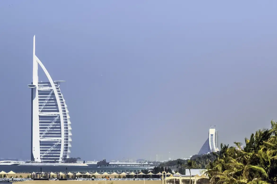 Sail-shaped skyscraper with distant hotel amid palm trees on sunny day