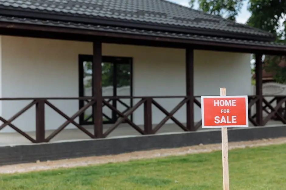 House with dark wooden porch and "Home for Sale" sign on green lawn