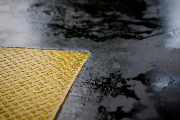 Wet textured yellow triangular floor sign on glossy dark pavement surface