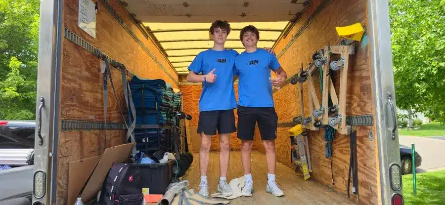 Two people in blue shirts standing inside an open moving truck with equipment around them