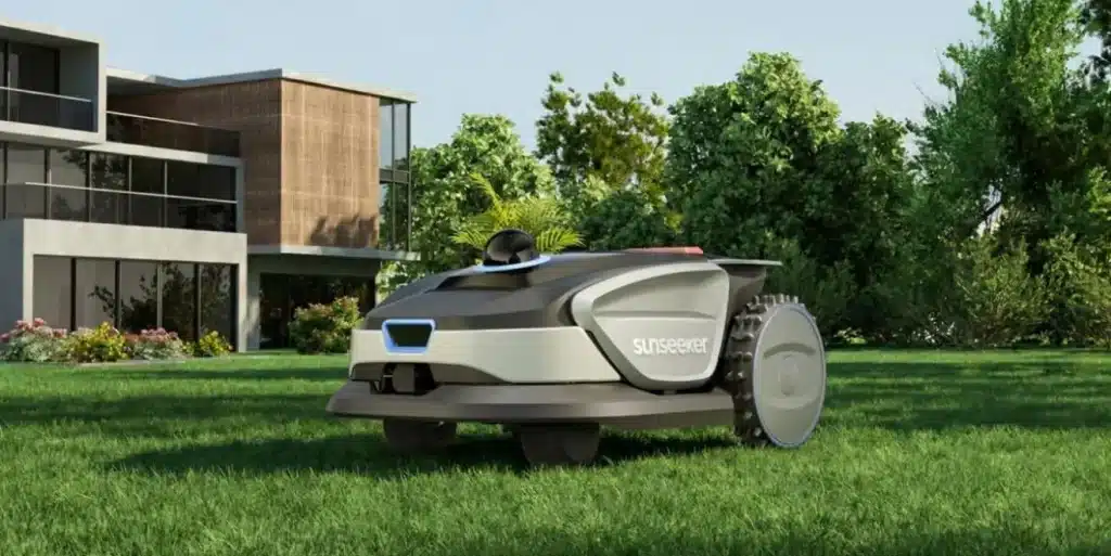 Robotic lawn mower on green grass near modern house with large glass windows in daylight