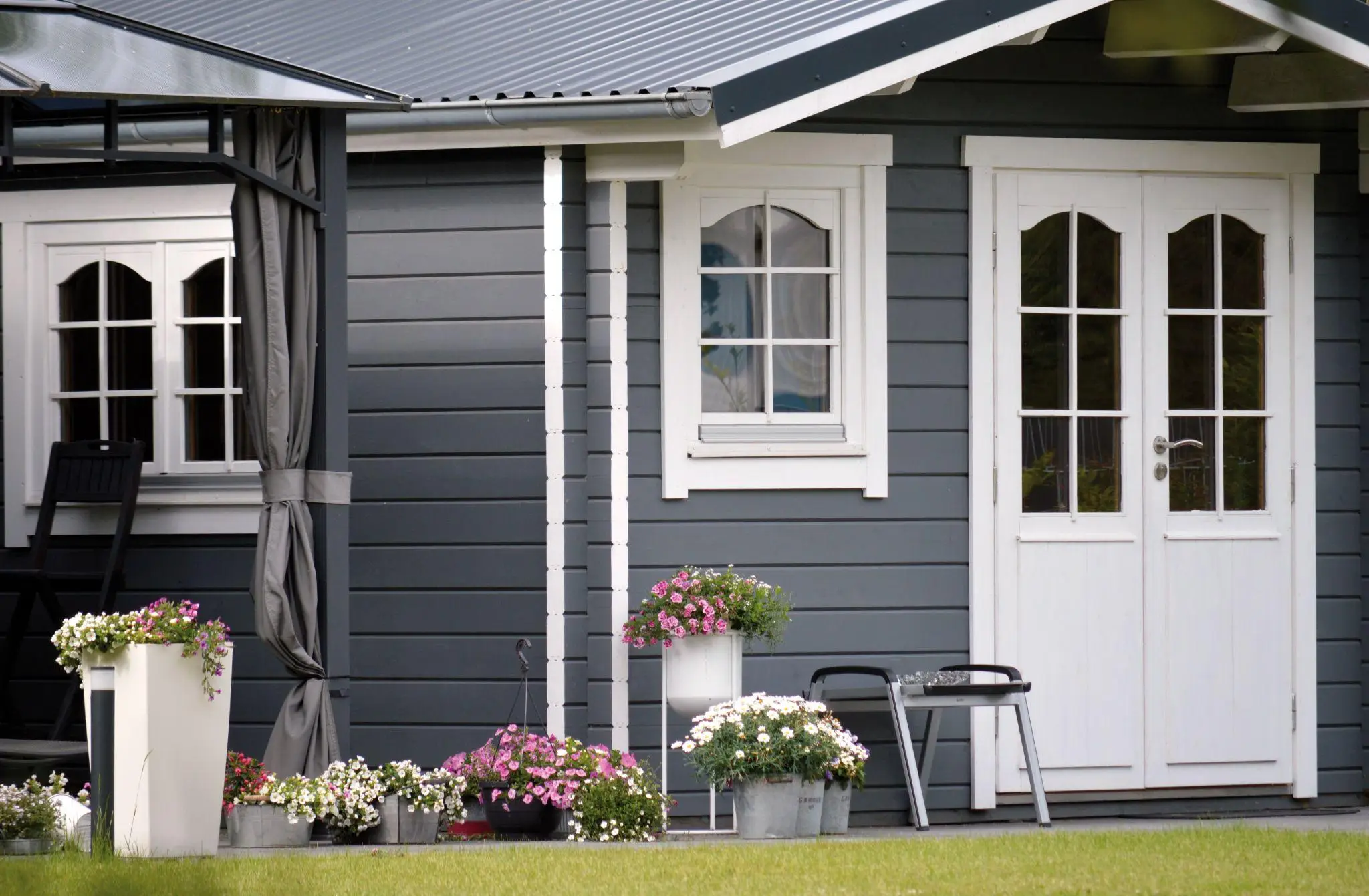 Blue wooden garden shed with white trim, surrounded by potted flowers in a grassy yard