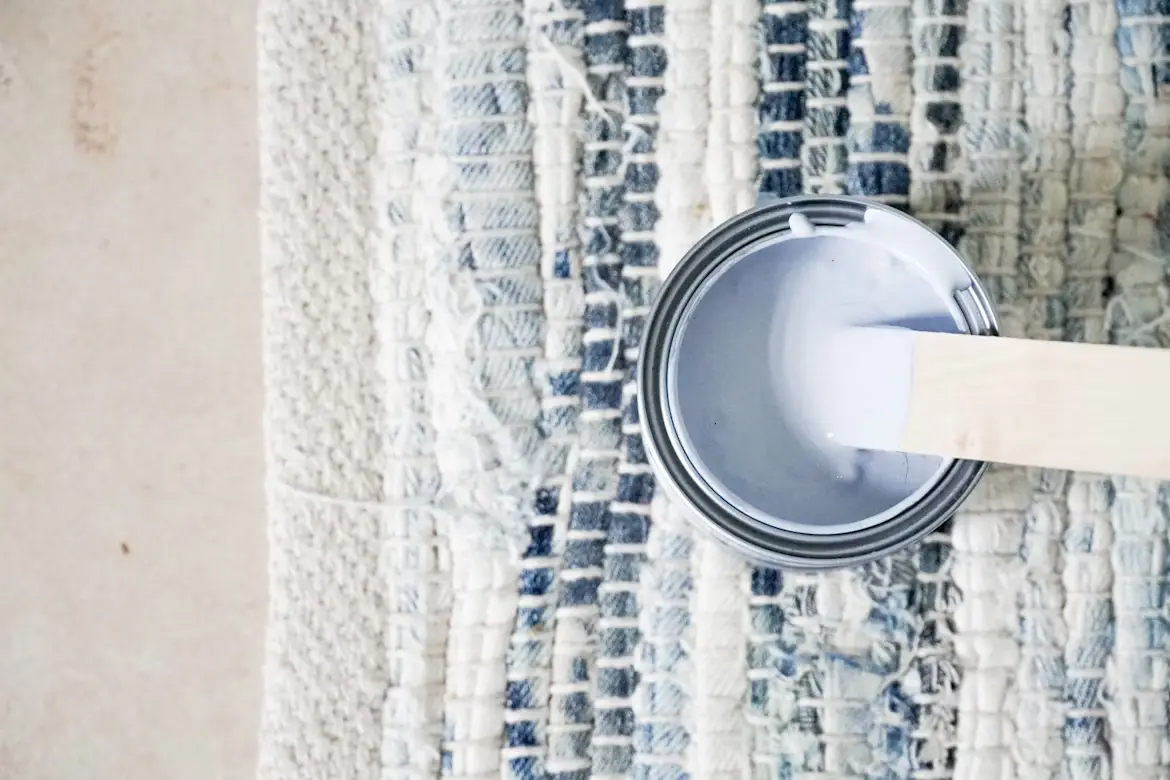 Open can of light blue paint with wooden stirrer on textured rug background