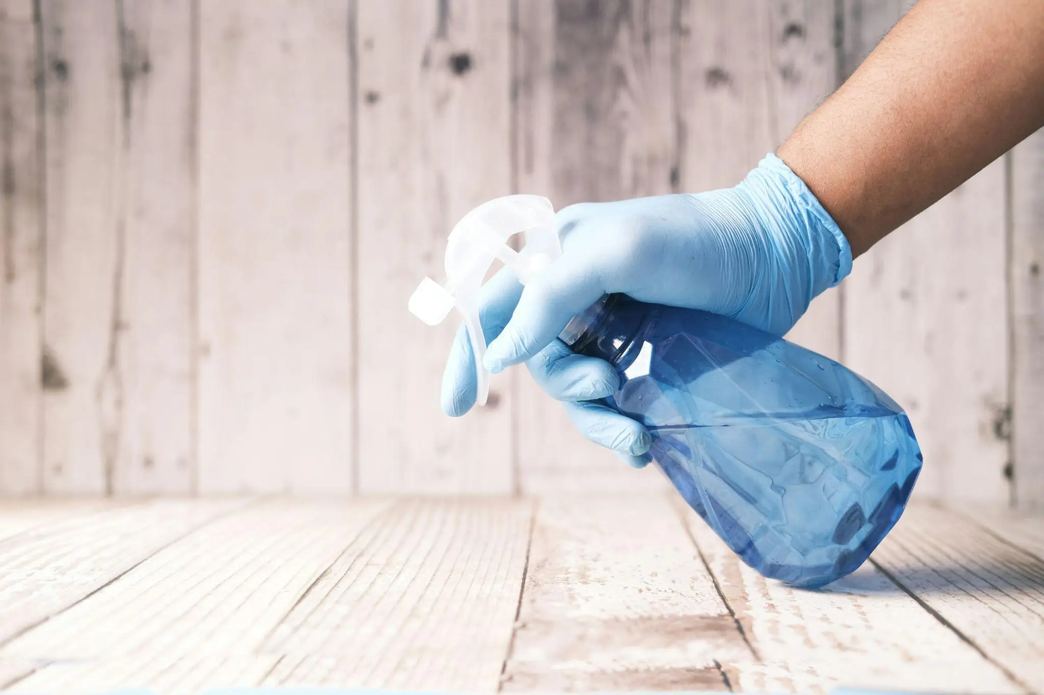 Gloved hand holding blue spray bottle on wooden surface
