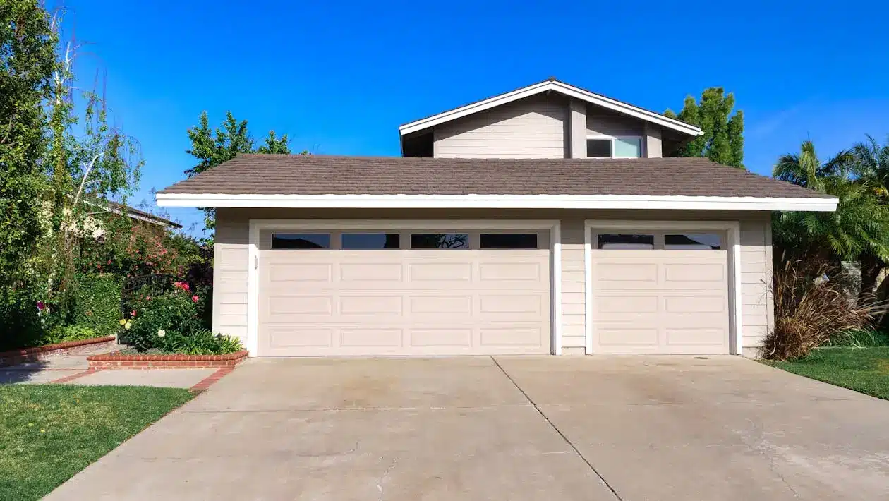 Two-car garage with beige doors in suburban setting under clear blue sky