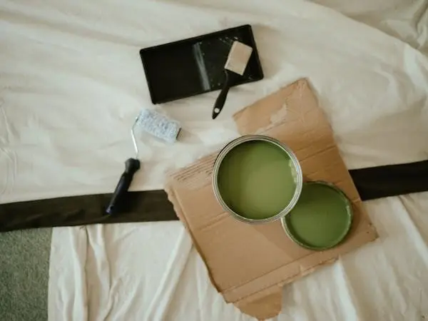 Paint cans with green paint on cardboard, alongside roller and brush on a white sheet