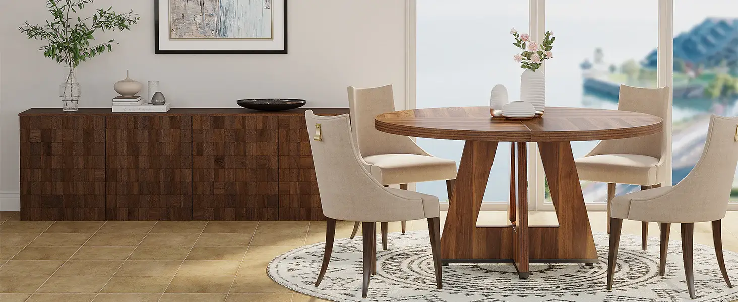Dining room with round wooden table, beige chairs, and sideboard against large windows and coastal view